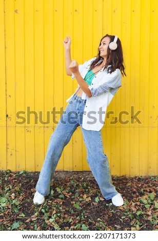A full-length view of a beautiful cheerful girl jumping while listening to a melody isolated against a bright yellow background. a young woman with headphones dancing on the street . generation z