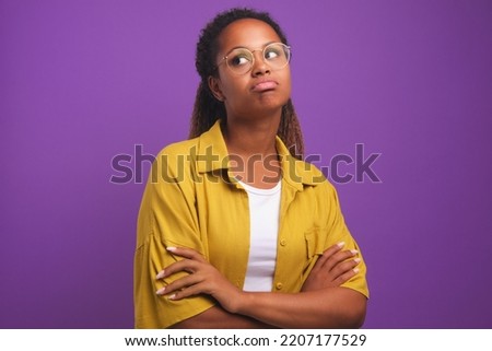 Young offended casual African American woman in round glasses hands crossed pouts lips and looks up after insults or quarrels with friends stands on plain purple background. Millennial, generation z Royalty-Free Stock Photo #2207177529