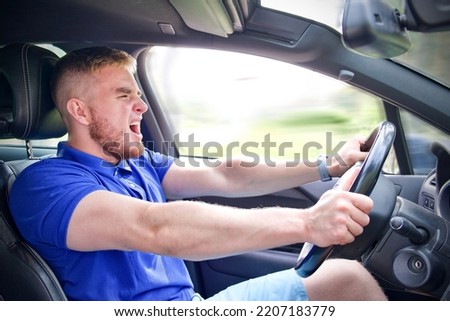 Handsome frightened angry guy, driver, young scared man shocked about to have accident, driving car fast on road holding steering wheel of automobile. Unfastened by a seat belt. Traffic violation Royalty-Free Stock Photo #2207183779