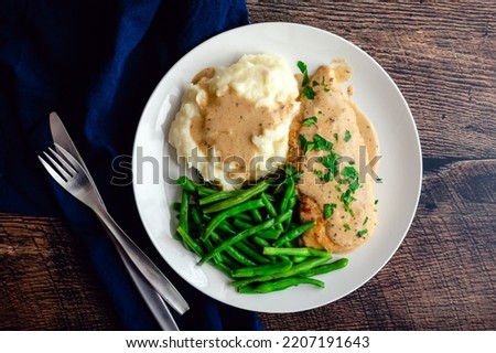 Chicken Breast Served with Green Beans, Mashed Potatoes, and Garlic Gravy: Chicken cutlet topped with creamy garlic sauce served with vegetables Royalty-Free Stock Photo #2207191643