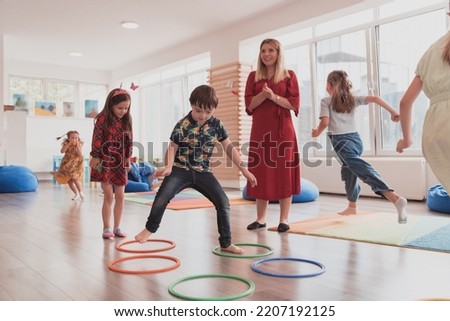Small nursery school children with female teacher on floor indoors in classroom, doing exercise. Jumping over hula hoop circles track on the floor. Royalty-Free Stock Photo #2207192125