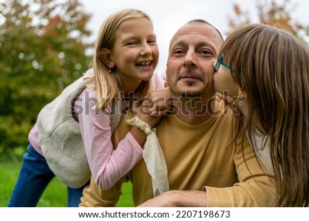 Portrait of a little girls kissing their dad on cheek. Pretty girls giving a kiss to their father outdoor. Adorable daughters kissing their happy father