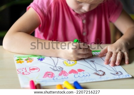 Child drawing a picture of her family with colored markers. Little girl, sitting at the table. Kid learning to draw
