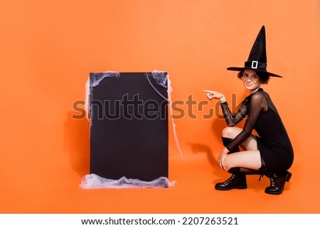 Full body photo of charming witch lady indicate finger empty space placard isolated on orange color background