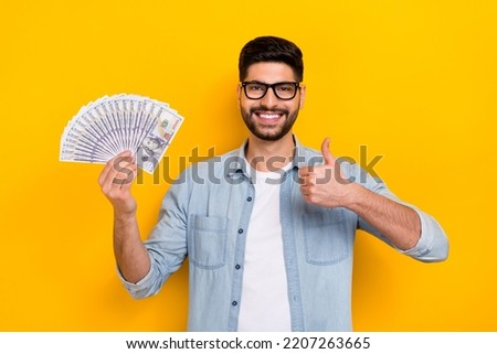 Photo of attractive man stylish trendy denim financial manager hold money show cool symbol isolated on yellow color background