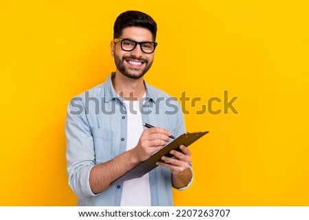 Portrait of young smiling happy man writing paper pad work document isolated on yellow color background