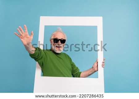 Photo of excited positive aged person hold paper album window arm palm waving isolated on blue color background
