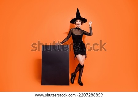 Full body portrait of delighted excited magician lady raise fist show empty space card isolated on orange color background