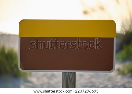 Empty signboard with copy space on seaside beach with small sand dunes and grassy vegetation on warm summer evening
