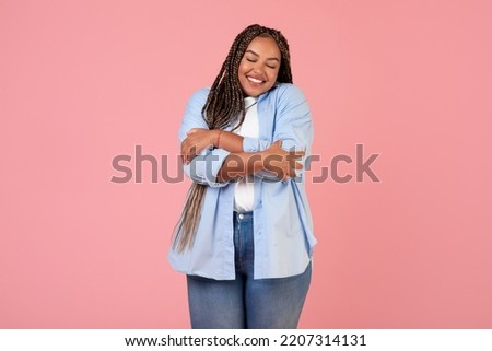 Body Positive. Happy African American Overweight Female Hugging Herself Posing With Eyes Closed, Wearing Plus Size Clothes Standing Over Pink Studio Background. Self Love Concept Royalty-Free Stock Photo #2207314131
