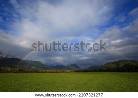 Weather picture in the Alps with full rainbow, clouds and blue sky