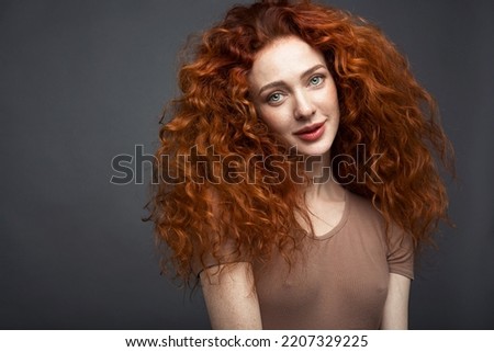 Portrait of a curly-haired red-haired woman on a dark gray background. The woman looks directly into the camera. With a space to copy. High quality photo