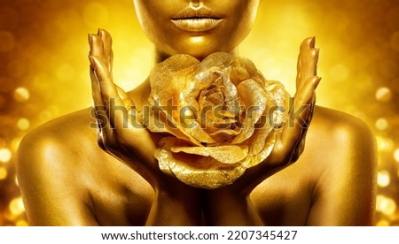 Gold Skin Woman Face. Golden Lips Make up with Flower close up. Female Hand Palms Holding Jewellery Rose over Shining Fantasy Background. Luxury Beauty Spa. Gold Metallic Bodyart