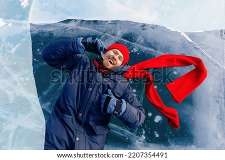Portrait happy male tourist in red hat with shard of transparent ice in winter on Lake Baikal sunset.