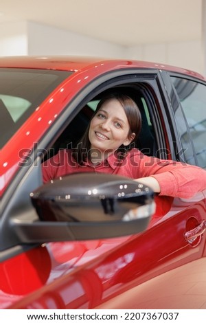 happy woman buys a red car at a car dealership. signing a trade-in contract and handing over keys, shaking hands. A successful woman chooses a new car. Rent a vehicle or repair service center.