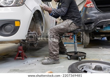 male working on car while sitting on creeper chair body repair panel beating sanding car  Royalty-Free Stock Photo #2207369481