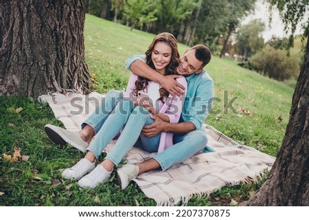 Photo of sweet cute boyfriend girlfriend wear casual outfits sitting grass hugging typing device enjoying sunny weather outdoors garden