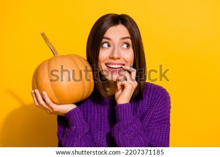 Photo of positive adorable minded lady hold pumpkin bite finger nail look empty space isolated on yellow color background