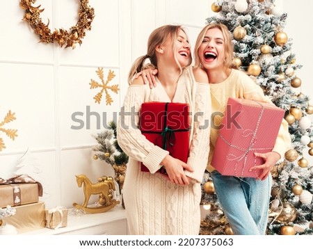Two beautiful blond women. Models posing near decorated Christmas tree at New Year eve. Having fun, ready for celebration. Bright holiday of best friends dressed in warm winter sweaters Royalty-Free Stock Photo #2207375063
