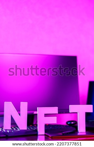 NFT inscription in pink neon light. NFT lettering at workplace with graphics tablet, smartphone and computer equipment. Copy space