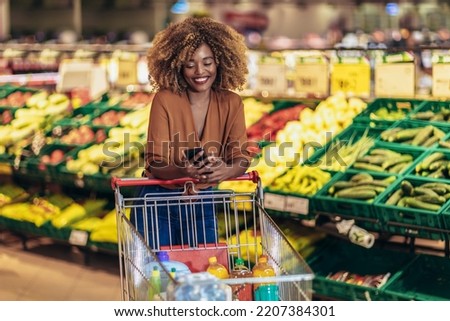 Cheerful African American Woman In Supermarket Choosing Fresh Grocery Using Phone