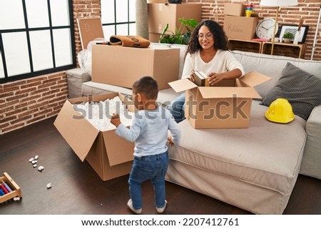 Mother and son unpacking cardboard box sitting on sofa at new home