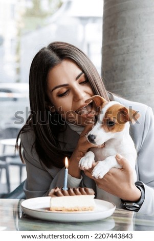 Caucasian woman and jack russell terrier look at the cake with a candle. The dog and the owner celebrate the birthday