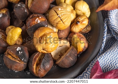 Roasted chestnuts in cast iron pan over rustic wooden board, selective focus.
