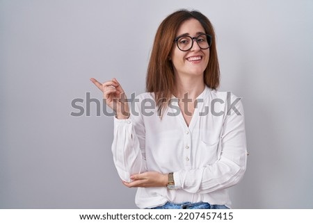 Brunette woman standing over white isolated background with a big smile on face, pointing with hand finger to the side looking at the camera. 