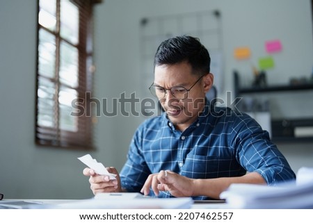 Portrait of a male SME business owner with a stressed and anxious face using a calculator to calculate expenses from the bill on hand and annual income tax to pay the Revenue Department.