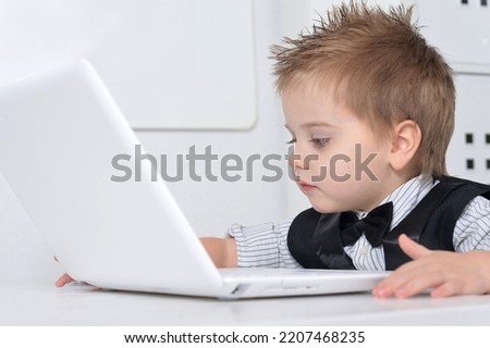 Little handsome boy sits with a computer at the table