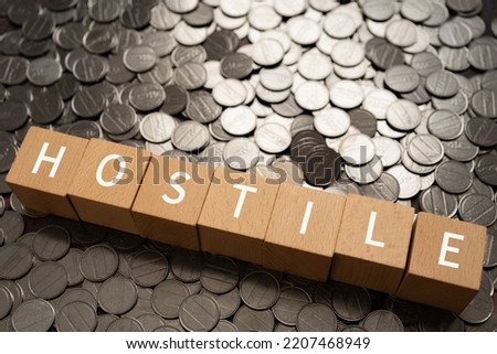 Wooden blocks with "HOSTILE" text of concept and coins.