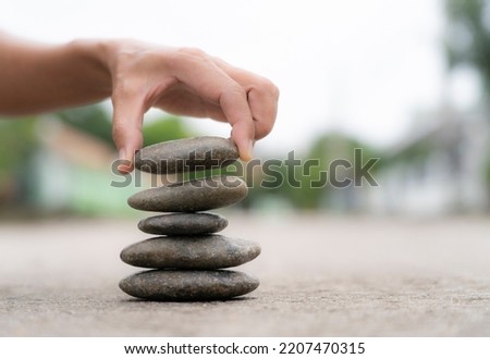 female hand holding stone for stack  on cement floor, . Pyramid pebbles free space. Calm, buddhism symbol or aromatherapy set concept.