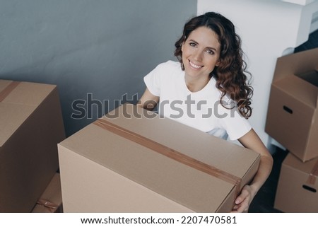 Smiling hispanic female homeowner tenant holding cardboard box parcel with things, preparing for garage sale or donation items to charity. Easy relocation. Advertising of moving or delivery service. Royalty-Free Stock Photo #2207470581