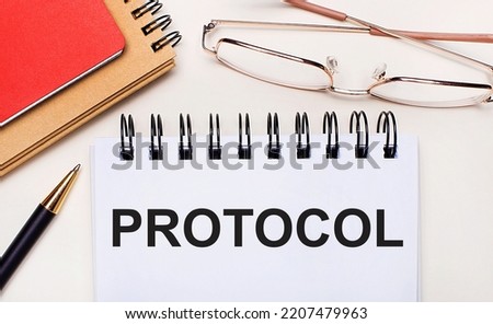 On a light background - glasses in gold frames, a pen, brown and red notepads and a white notebook with the text PROTOCOL. Business concept