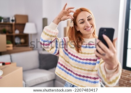 Young caucasian woman having video call holding key at new home