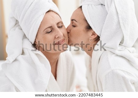 Mother and daughter wearing bathrobe kissing at bedroom