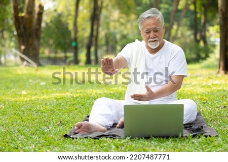 asian senior man workout and doing yoga with online training from laptop computer in the park