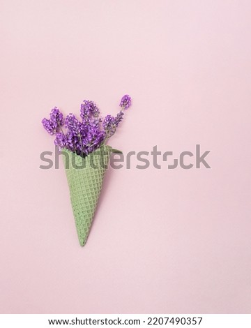 Green ice cream cone filled with blooming purple lavender flowers on pastel pink background. with copy space Idyllic summer aesthetic. Minimal concept of sweet ice cream refreshing flavor.