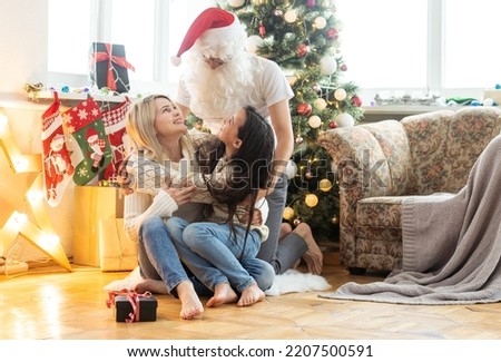 Picture of happy family celebrating New Year eve, little girl with parents enjoying winter holidays, father wearing Santa Claus costume, Christmas magic, happiness and love concept