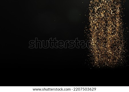 Shiny golden glitter falling down on black background, space for text. Bokeh effect