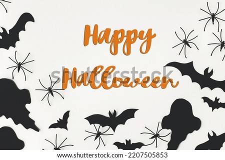 Happy Halloween text on black ghosts, spiders, bats on white background flat lay. Happy Halloween! Creative greeting card, handwritten sign. Trick or treat!