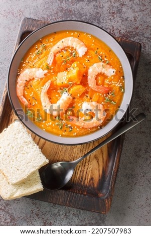 spicy pumpkin and shrimp soup with sesame and thyme closeup in the bowl on the table. Vertical top view from above
