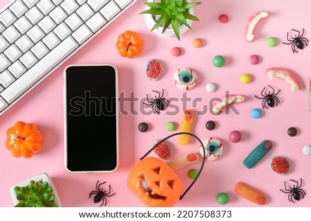 A smartphone with a blank screen on a background of various sweets on a pink background. Happy Halloween. Space for copying. Flat position, top view.