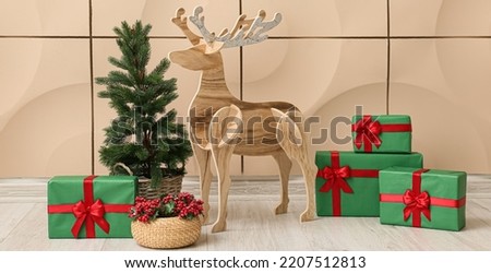 Wooden reindeer with Christmas tree, mistletoe and presents near beige wall in room