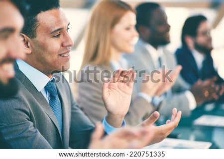 Young business partners applauding at seminar, focus on smiling man