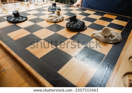Traditional Georgian dish, khinkali Kalakuri, on wooden table, chess board, rustic, side view, black and light dough, playing chess. Selective focus, side view. Meat and cheese dishes