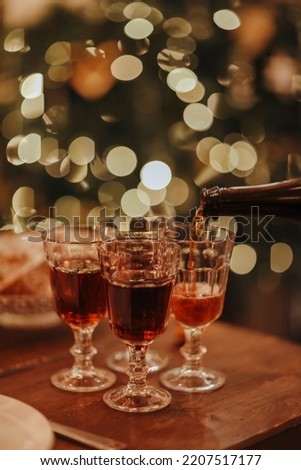 New Years Eve celebration. Man pouring champagne into glasses standing on table with festive xmas dinner, candles and wrapped gifts against blurred background and firtree, cropped