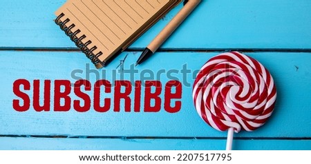 Subscribe concept. Stationery and lollipop on blue wooden background.