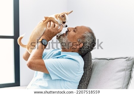 Senior grey-haired man smiling confident holding chihuahua at home